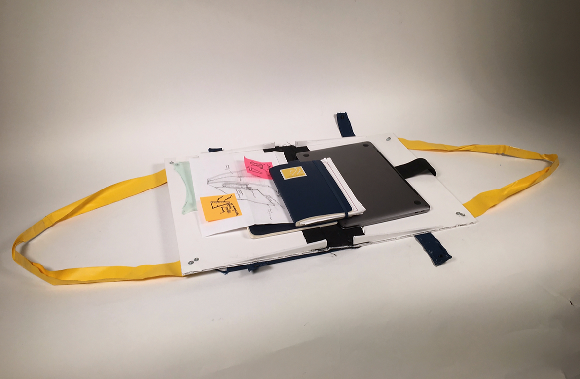 A prototype for a bag that opens all the way flat, with a laptop, charger, and some papers to demonstrate fit.