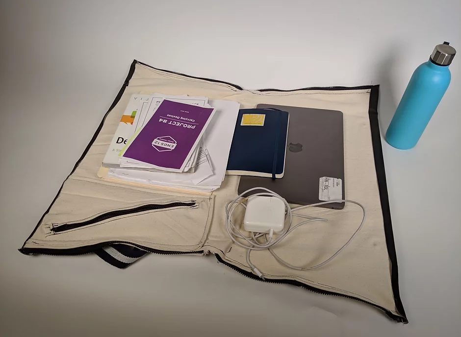A prototype for a bag that opens all the way flat, with a laptop, charger, and some papers to demonstrate fit.